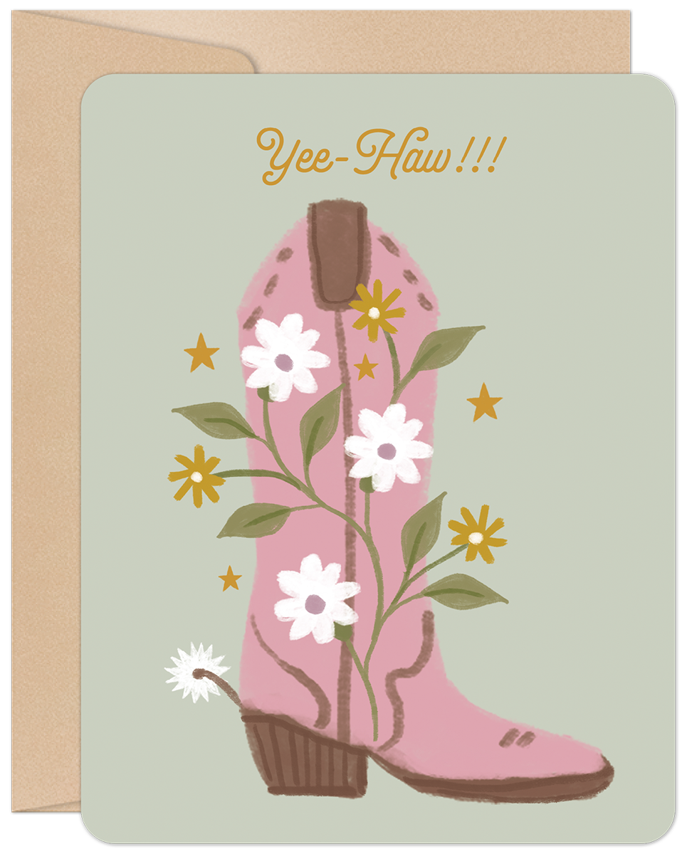 Front of an encouraging birthday greeting card featuring a pink cowboy boot adorned with white and yellow daisies, green vines, and gold stars on a light green background, with 'Yee-Haw!!!' in orange script. A kraft paper envelope is visible behind the card.