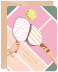 Greeting card featuring two hands holding pickleball paddles with floral and striped designs, a pickleball, and the pun text 'I DINK YOU'RE THE BEST' on a pastel geometric background. Includes a kraft envelope.