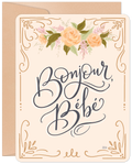 Elegant greeting card for a new arrival featuring 'Bonjour, Bébé' in sophisticated calligraphy, adorned with soft peach roses and gold botanical details, paired with a kraft envelope. Perfect for welcoming a little one.
