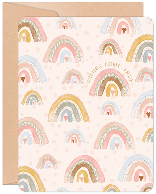 Cute new baby greeting card with watercolor rainbows, hearts, and "Wishes Come True" text, on a craft paper envelope.