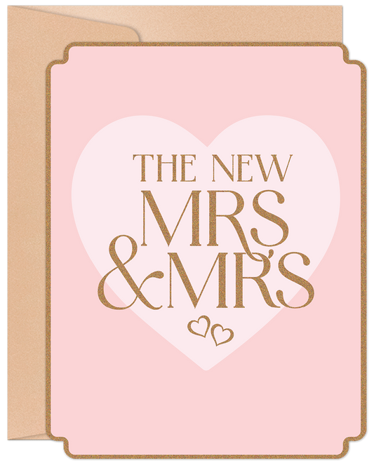 Front of a light pink wedding card with 'THE NEW MRS & MRS' in shimmering gold letters inside a white heart design, celebrating two brides.