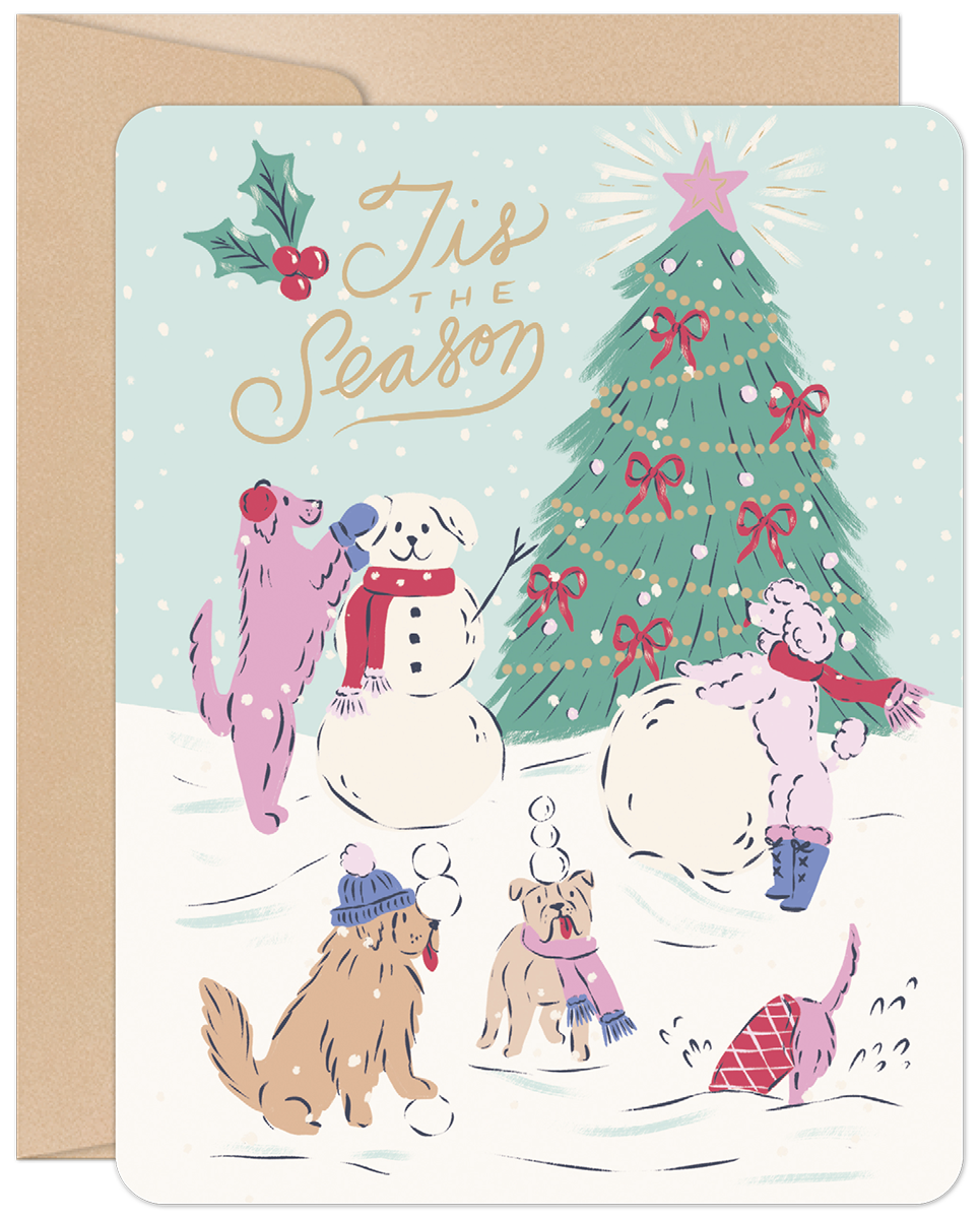 Whimsical Christmas greeting card featuring five cartoon dogs playing in the snow, building a snowman, and admiring a decorated Christmas tree with a star. Holly and 'Tis the Season' text are visible. Card has rounded corners and a brown envelope.