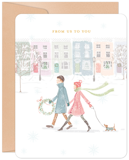 Front of a vintage sparkle Christmas card showing a couple walking a dog through a snowy village with 'FROM US TO YOU'.