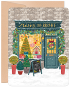 Illustrated holiday greeting card featuring a charming winter storefront adorned with festive garlands, a glowing 'Merry and Bright' sign, a decorated Christmas tree, gingerbread house, and gifts in a snowy setting.