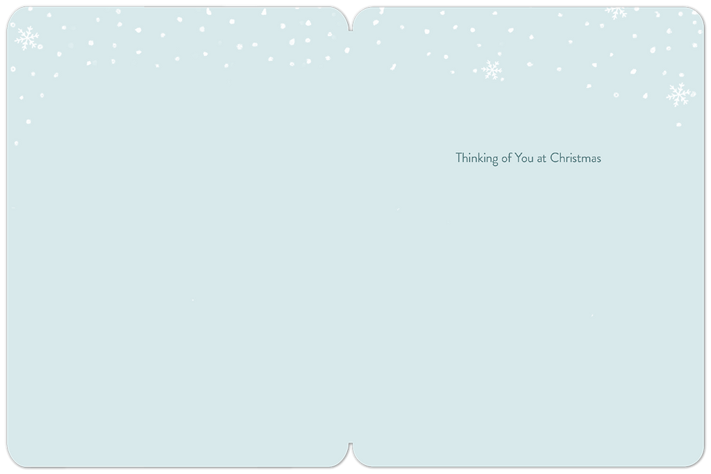 Inside of a holiday greeting card with a light blue background, subtle falling snowflakes, and the heartfelt message 'Thinking of You at Christmas' centered on the right page.