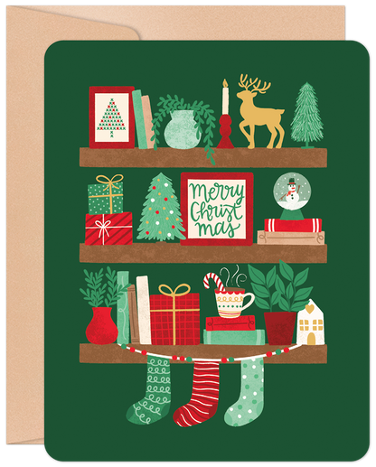 Front of a deep green Christmas card showcasing a charming bookshelf filled with festive decorations: gifts, a tree, reindeer, and 'Merry Christmas'.