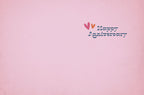 Inside of a romantic greeting card with a simple 'Happy Anniversary' message in blue text, accented by small pink and orange hearts, on a soft pink background. Perfect for a spouse.