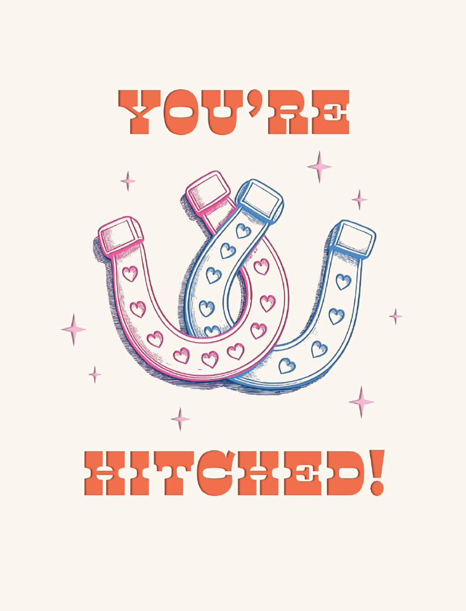 Front of a cute wedding greeting card with 'YOU'RE HITCHED!' in bold orange text, featuring two interlocking pink and blue horseshoes adorned with small hearts and surrounded by tiny sparkling stars.