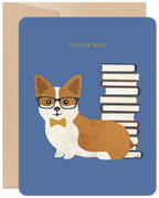 Front of a blue graduation greeting card featuring a cute, bespectacled corgi wearing a yellow bow tie, sitting next to a stack of books with the text 'CLEVER BOY!' above.