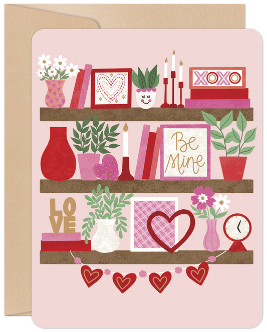 Front of 'Be Mine' Valentine's Day card featuring charming shelf decor with hearts, potted plants, books, candles, and 'XOXO' and 'LOVE' accents.