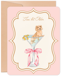 Front of a funny birthday greeting card featuring a cute golden dachshund puppy sitting in a martini glass with a lemon twist, on a light pink background with an ornate gold frame. Text reads "'Tini bit Older".