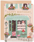 Whimsical patisserie birthday greeting card featuring a charming Parisian street scene with flower boxes, buzzing bees, delightful animals including a dog and cat, and a sweet shop storefront, perfect for celebrating special occasions.