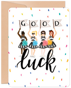 Front of an encouraging greeting card featuring four diverse female cheerleaders in black and white striped outfits holding 'GOOD' flags and colorful pom-poms, surrounded by confetti, with 'luck' in script below. Perfect for friends embarking on new journeys.