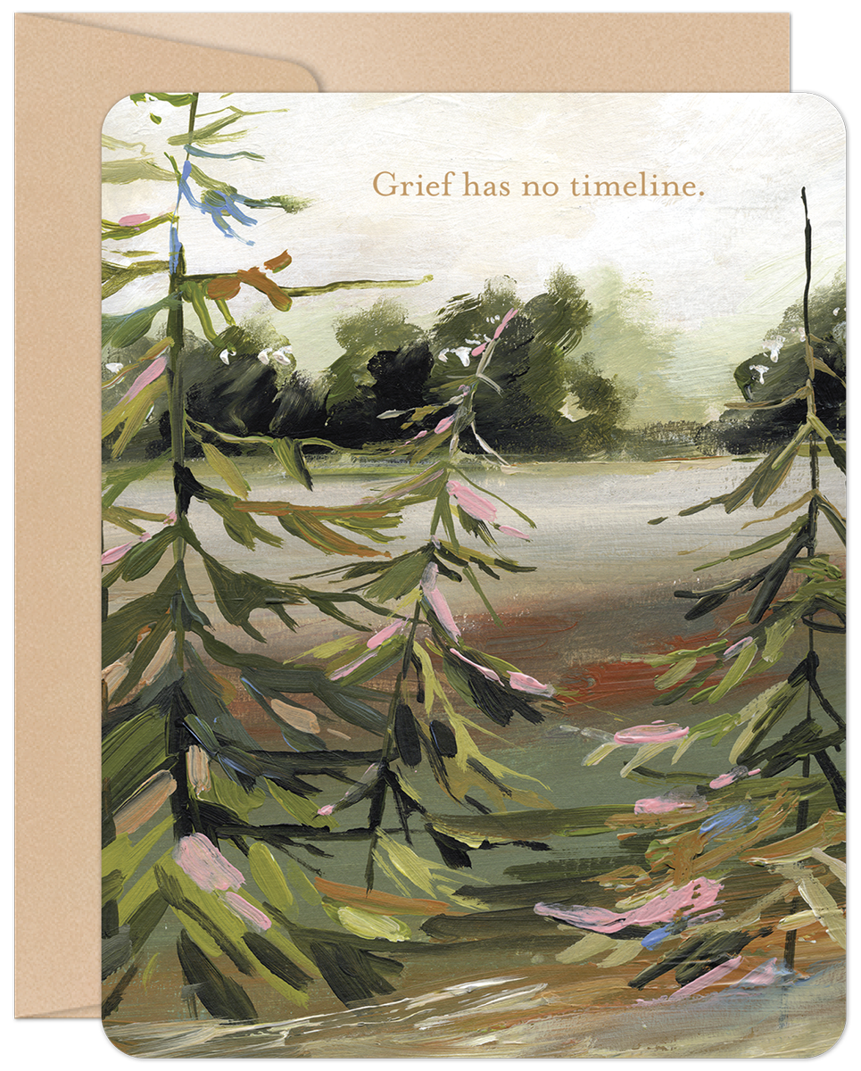 Front view of a comforting nature-themed greeting card featuring an impressionistic painting of lush green pine trees and a calm body of water, with the subtle text 'Grief has no timeline.' A kraft brown envelope is partially visible behind the card.