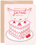 Romantic birthday greeting card with a heart-shaped pink cake, cherries, and 'Wishing you a sweet Birthday' banner on a light background with kraft envelope.