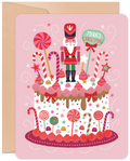 Pink festive greeting card featuring a decorated white cake with a nutcracker, candy canes, lollipops, stars, and 'Merry Christmas' text.