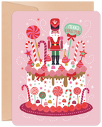 Pink festive greeting card featuring a decorated white cake with a nutcracker, candy canes, lollipops, stars, and 'Merry Christmas' text.