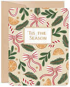 Front of a festive holiday greeting card featuring a pattern of red and white striped bows, candy canes, evergreen branches, and dried orange slices on a beige background. The card reads 'Tis the Season in the center, with a kraft paper envelope peeking from behind. Ideal for sending season's greetings.