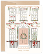 Front of a charming cream-colored holiday card featuring an illustrated house adorned with festive garlands, string lights, ornaments, and red bows, perfect for sending seasonal greetings.