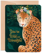 Front of a greeting card featuring an elegant leopard with teal eyes, adorned with a vibrant flower crown, surrounded by lush jungle foliage. The card displays the warm message 'You're Wild and Wonderful' in stylish script, perfect for a special anyone.