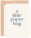 Elegant white greeting card with vertical gold pinstripes and navy text 'a little paper hug', peeking from a kraft brown envelope. Perfect for sending love and comfort.