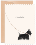A cream-colored greeting card with scalloped edges, featuring a whimsical illustration of a black Scottish Terrier dog looking up at a dotted line forming an arc, with the text "a little hello" above. The dog wears a pink collar. A kraft envelope peeks out from behind the card.